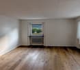empty room with wooden floor, white walls, radiators, windows with white curtains