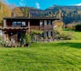 wooden chalet, large green lawn, trees, mountains in the background
