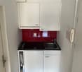 modern kitchen with white cabinets, red backsplash, black countertop, stainless steel sink, faucet, electrical outlet, and a small open cabinet with a washing machine