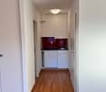Empty kitchen with white cabinets, wooden floor, sink, faucet, and a small window