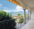Covered balcony with ornate wrought-iron railing, overlooking a scenic view of mountains and a body of water