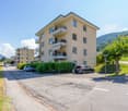 3-story apartment building with yellow exterior, balconies, and parking spaces in front