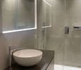 modern bathroom with gray tiles, white sink, mirror, and glass shower enclosure