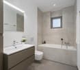 Bathroom with modern design, bathtub, toilet, vanity, and white tile walls.