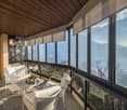 spacious balcony, large windows, modern white seating, table, beautiful view of the ocean and mountains