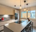 modern kitchen with light grey cabinets, tiled countertops, integrated appliances, central island with dining chairs, pendant lights, large window with city view