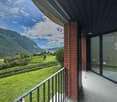 Outdoor balcony, glass wall, black railing, tiled floor, expansive view of the countryside with mountains, greenery, and a river
