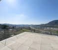 A rooftop terrace with glass railings, tiled floor, and a beautiful view of the cityscape.