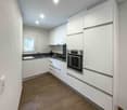 modern white cabinetry, wooden floors, white walls, integrated dishwasher, washing machine, electric stove, oven