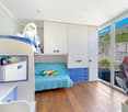child's bedroom with bunk beds, colorful sofa, wardrobes, windows, stuffed animal, pillows, bookshelf