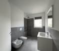 Minimalistic bathroom with white sink, gray tiles, separate shower and toilet, small window