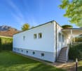 White house, modern architecture, raised ground floor, windows, stairs, garden with plants and trees, mountain in the background