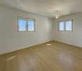 Empty room with white walls, wooden floor, two windows, and mountain view