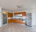 Open kitchen with granite countertops, wooden cabinets, modern appliances including a dishwasher and washing machine, white tiled floor, neutral color palette, ample natural light from windows