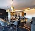 modern design dining area with gold chandeliers, black marble floors, large oval glass table, leather chairs, white walls, built-in shelves, and a large painting