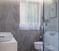 modern bathroom with marble tiles, white fixtures, glass shower enclosure, white vanity with double sinks, toilet, bidet, and a window with white curtains