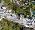 Under construction 3 stories house with brown roof, solar panels, surrounded by houses, small garden, road, parking area, crane