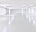 Large open-plan commercial space with white walls, white ceiling, and white concrete floor. The space has several white columns supporting the ceiling and appears to be a vacant office or studio space.