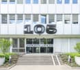 Modern office building with large windows, white facade, and prominent address number '105' displayed on the front.