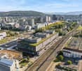 Urban area with numerous buildings, railway tracks, greenery, mountain range in the distance
