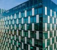 Modern multi-story building, glass exterior, reflective surfaces, vertical lines, clear skies, neighboring buildings, distant city skyline