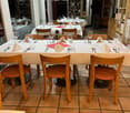 restaurant interior, large dining table set for multiple guests, shelves with wine bottles, white tablecloths, orange chairs, tiled floor