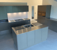 modern kitchen with gray cabinetry, stainless steel countertops, induction cooktop, kitchen island with sink and faucet, appliances in the right side