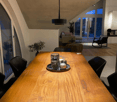 wooden table, 6 chairs, wooden floor, large windows, chandelier, indoor plants