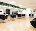 hairdresser's room with reception desk, hairdressing chairs, lounge chairs, hanging frames on wall, shelves, plants
