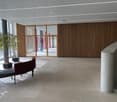 Open area with wooden wall and large window, a bench, and a plant.
