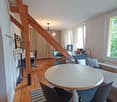 Living room with wooden floor, exposed wooden beams, round table with chairs, couch, monitor, windows, radiator, table with chair