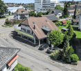 Aerial view of houses, trees, gardens, solar panels, street, parked cars, and building with swimming pool