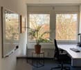 Empty office room with white walls, windows, desk, chair, computer, monitor, lamp, potted plant, whiteboard, picture frame, radiator.
