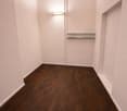 an empty room with wooden flooring, white walls, a single light fixture, and a small glass shelf on the right side