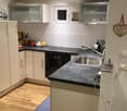 modern kitchen with a granite countertop, stainless steel sink, white cabinets, wooden floor, and built-in appliances