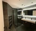 modern bathroom with gray walls, glass shower, double sink, large mirror, towel rack