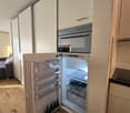 Open refrigerator with wine bottles, white cabinets, wooden floor, built-in oven, dishwasher