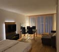 Bedroom with bed, TV, dining table, chairs, couch, side table, curtains, wooden floor
