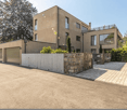 Modern house, beige exterior, large windows, garage, driveway, stone wall, greenery