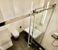 modern bathroom with white tiles, glass shower, white sink, white toilet, silver shower head
