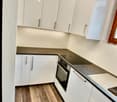 modern kitchen with white cabinets, wooden floor, black countertop, built-in oven, dishwasher, sink