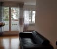 Black leather couch, glass doors leading to balcony, curtains, wooden floor, cane on right