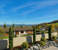 A view of a house with a terrace, rocks, and grass in front of a clear sky and mountains in the background