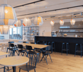 dining area with round tables and chairs, a bar counter, modern pendant lights, a coffee machine, a white couch, and decorative shelves