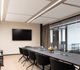 Large meeting room with modern furniture, black table, chairs, television, white walls, bright light.