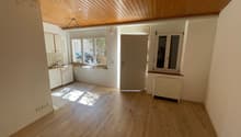 empty room, wooden floor, white walls, wooden ceiling, kitchen area with sink, cabinets, and windows