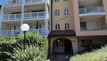 A two-story apartment building with several balconies, white railings, and a brick walkway.