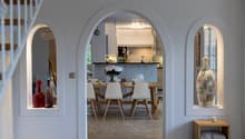 open floor plan with dining area and kitchen, white walls, brick floor, modern furniture, two windows with niches, stairs