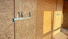 Interior of a storage shed with wooden floor, metal doors, and particleboard walls.