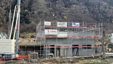 Construction site of a house in progress, surrounded by scaffolding, featuring large windows and door frames, a crane is present to lift materials